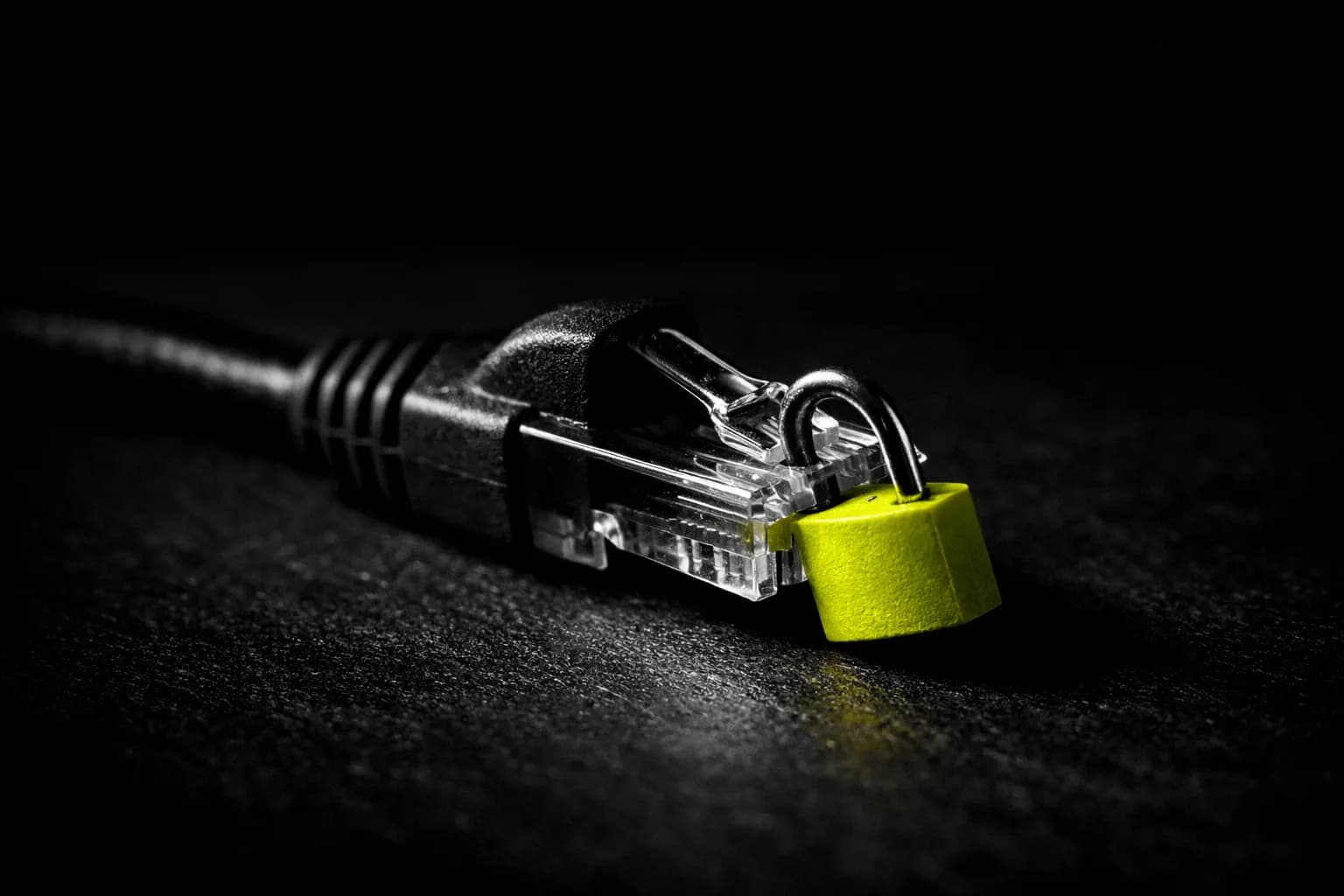 A grounded, dimly-lit scene of a locked ethernet cable sitting unplugged on a plain desk in a glass-walled office, with late…